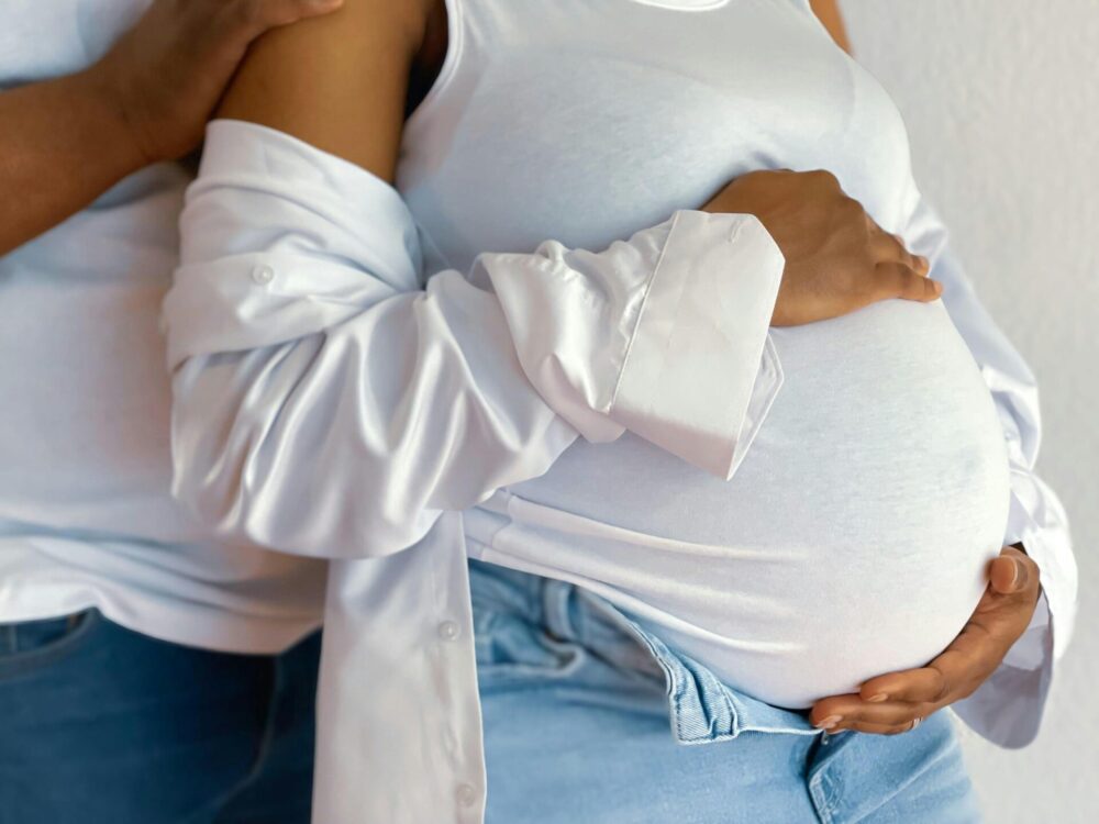Pregnant women with a partner standing behind her, close up on the belly